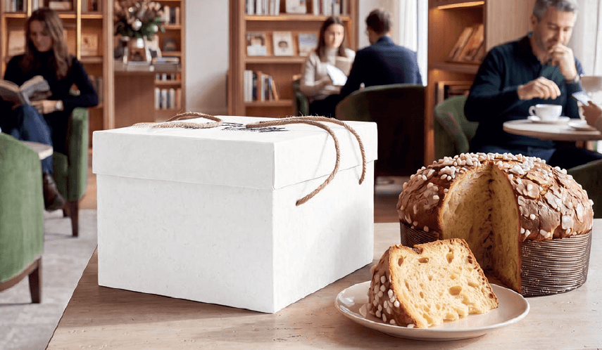 Cappelliera alta bianca con cordoncino accanto a un panettone tagliato